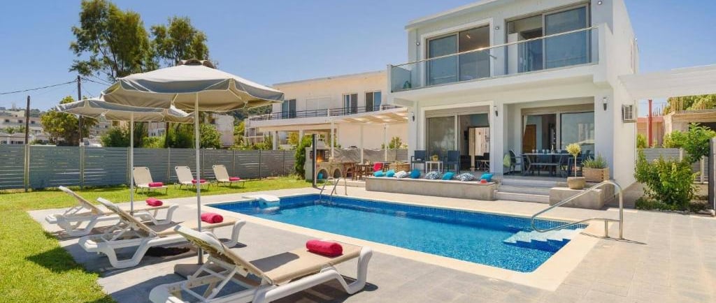 Modern luxury villa with a private swimming pool, sun loungers, and patio umbrellas on a sunny day.