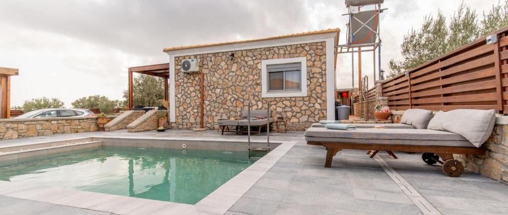 Luxury stone villa with a private swimming pool and cushioned sun loungers on a modern patio.