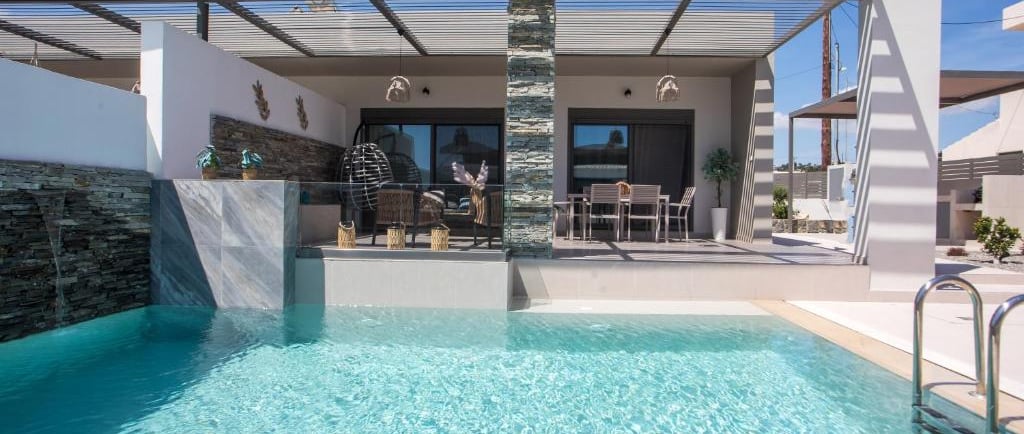 Modern luxury villa with a private turquoise swimming pool, outdoor dining area, and shaded patio.