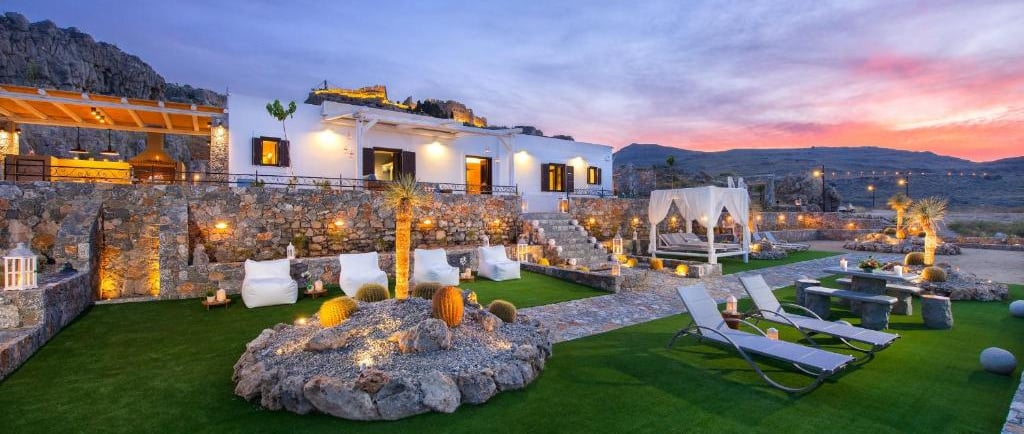 Luxury Mediterranean villa with stone walls, garden lounge, and sunset view over hills.