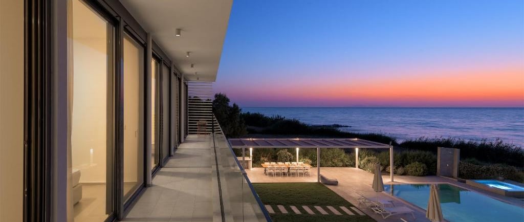 Luxury modern villa balcony overlooking a swimming pool and ocean at sunset.
