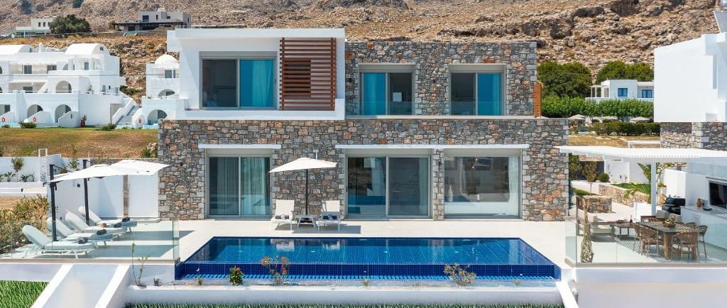 Luxury stone villa with a private infinity pool and sun loungers overlooking a mountain in Greece.