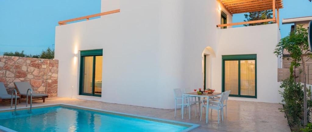 Modern Greek luxury villa with private pool, patio dining, and white architecture at dusk.