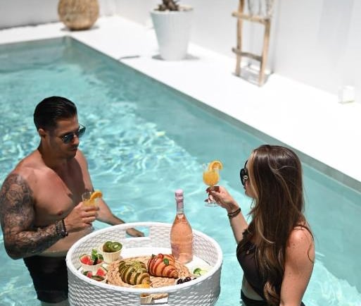 A couple enjoys a luxury floating breakfast tray with cocktails in a private pool.