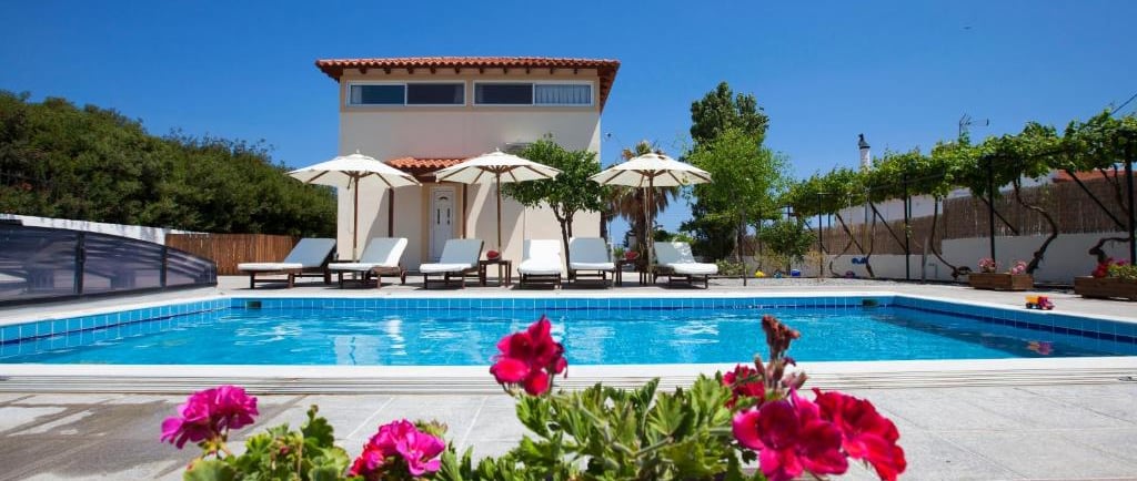 Luxury vacation villa with private swimming pool, sun loungers, and patio umbrellas under a clear blue sky.