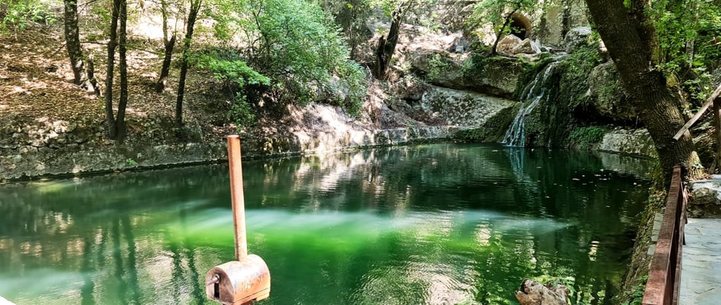 A tranquil green lake at the butterfly Valley in Rhodes, featuring a small waterfall and forest.