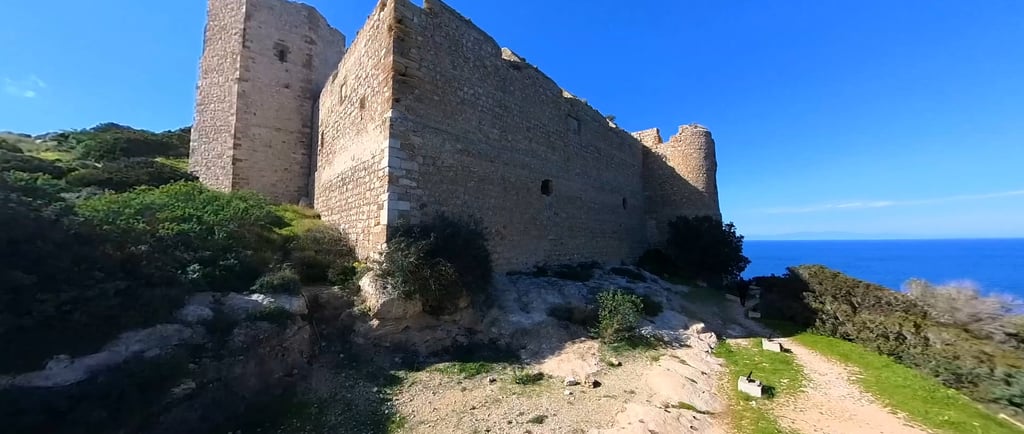 Medieval stone castle ruins overlooking the deep blue Mediterranean Sea under a clear sky.