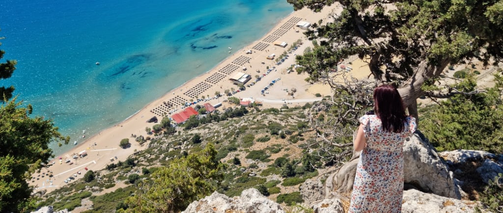 a woman watching tsambika beach from hilltop