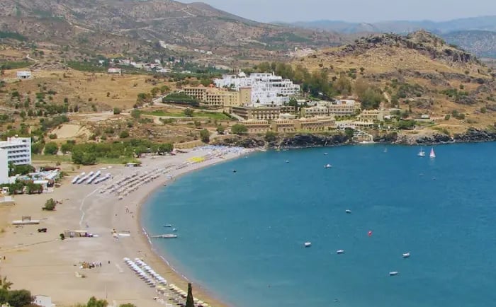 Aerial view of a sandy beach cove with luxury resorts and blue ocean water in Rhodes, Greece.