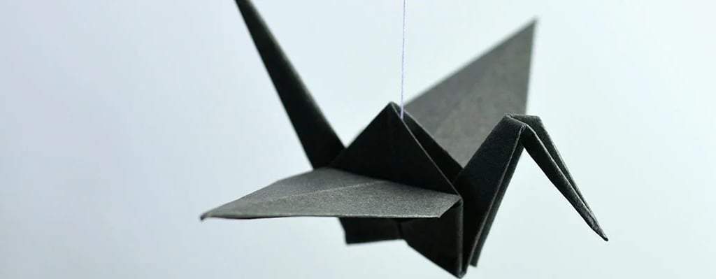 Una gru nera fatta con gli origami su sfondo azzurro