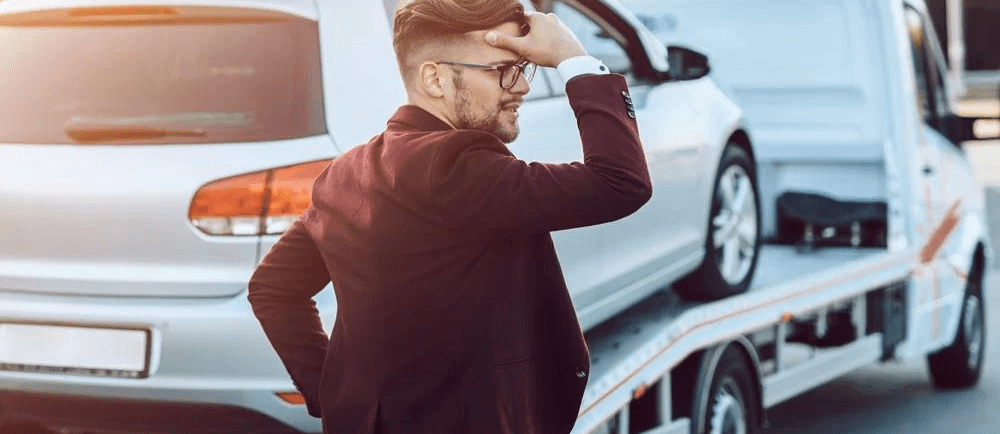 carro ao fundo em cima do guincho sendo apreendido e seu dono na frente preocupado