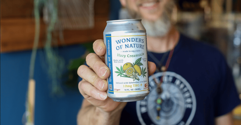 a man holding a can of  soda by wonders of nature.