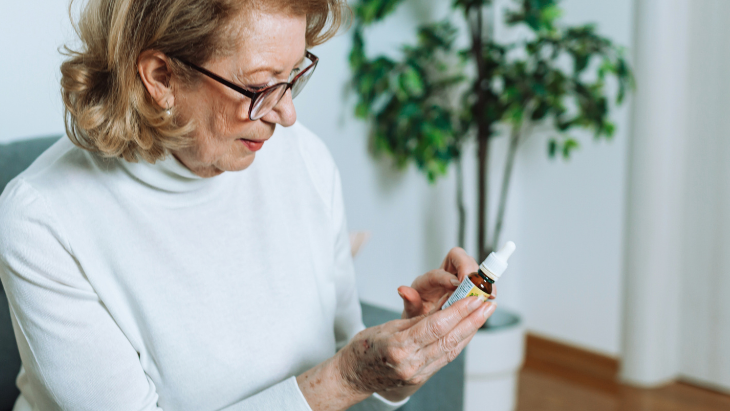 a woman in a white sweater and glasses is holding a bottle of CBD