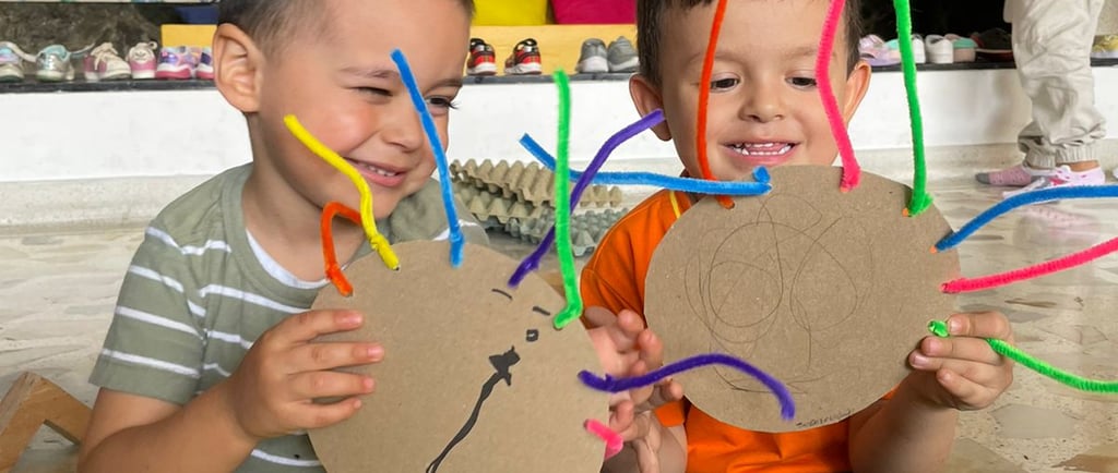 Niños mostrando obras de artes propias hechas con materiales reciclables en jardín Infantil Ukelele