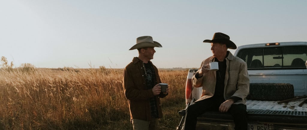 two men in cowboy hats sitting and standing next to truck drinking coffee at sunrise