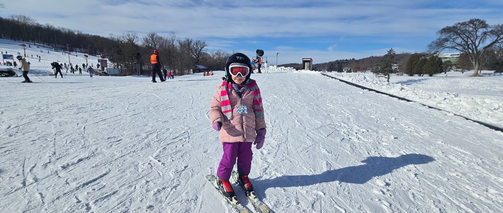 IMage of young girl with pink coat, purple pants, black helmet on skis