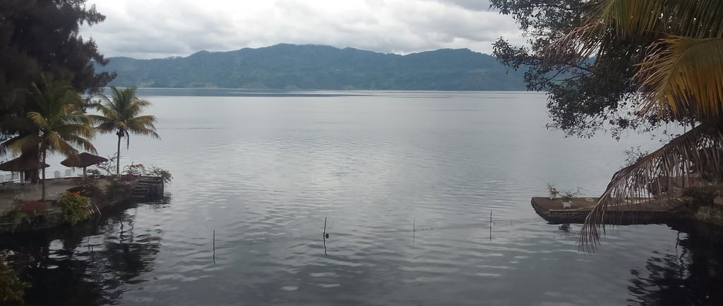 a still calm lake with mountains in the background and trees bordering the image
