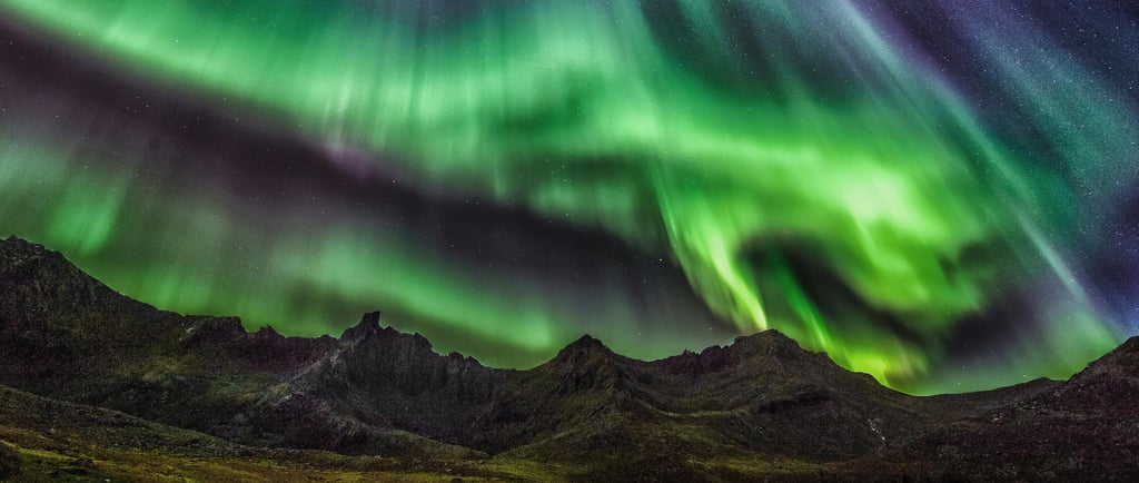 the northern lights appearing in green over a rugged mountainous landscape