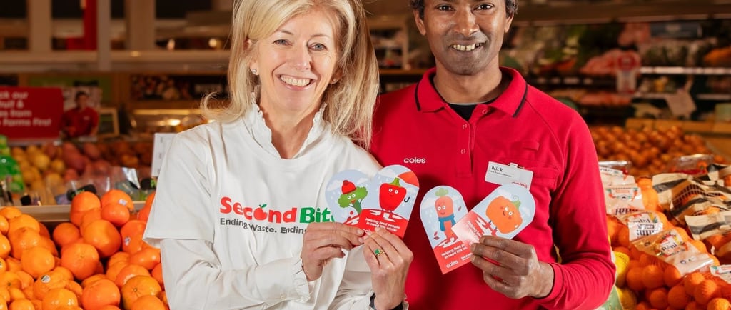 a man and woman holding up a sign that says,'Coles SecondBite winter appeal