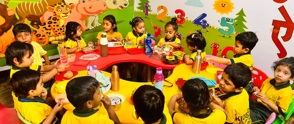 Preschool children in yellow uniforms eating lunch at a colorful table in a decorated classroom.