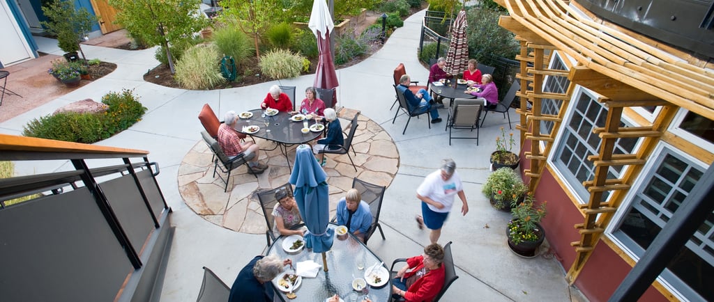 Groups of neighbors enjoying an outdoor meal at several tables on a patio.