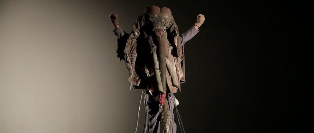 David Noir levant les bras dans son costume de pachyderme de "Défense du masque Ulin"