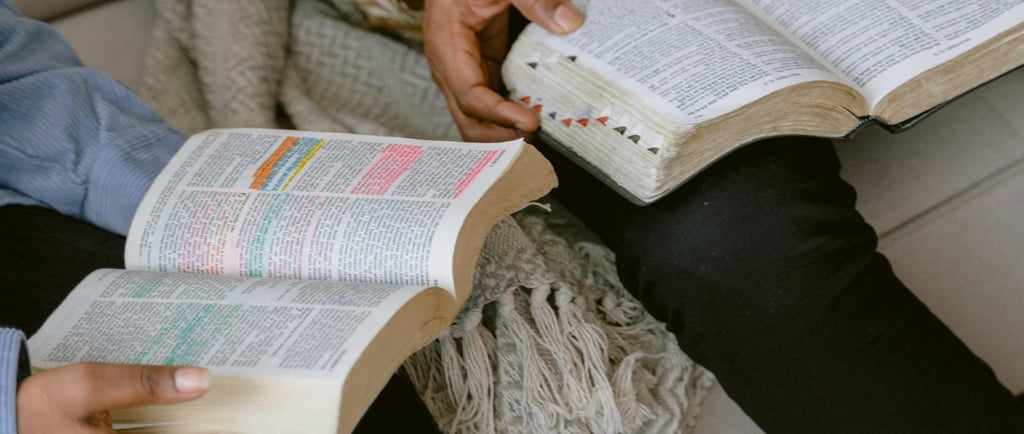 two people sitting and reading a bible in hand