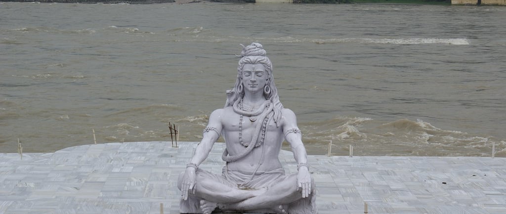 photo of a statue of Lord Shiva next to Ganges River