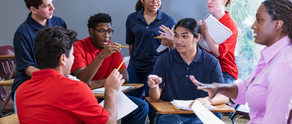 Diverse high school students engage in a group discussion with their teacher in a classroom setting.
