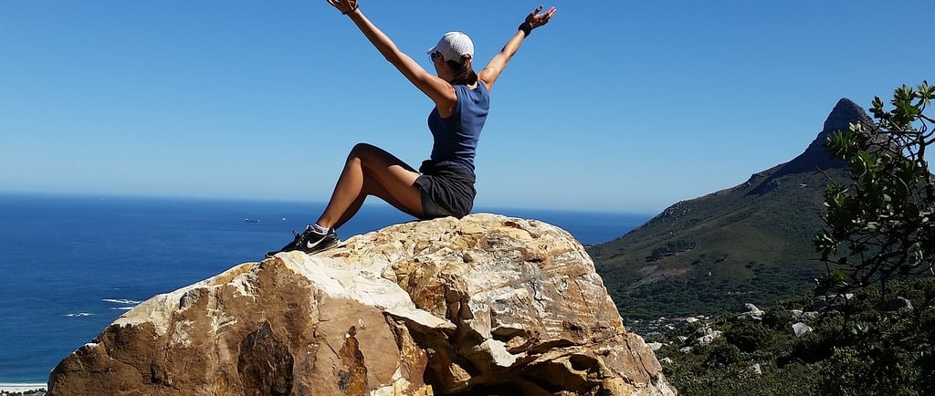 a woman sitting on a rock with her arms up and arms up