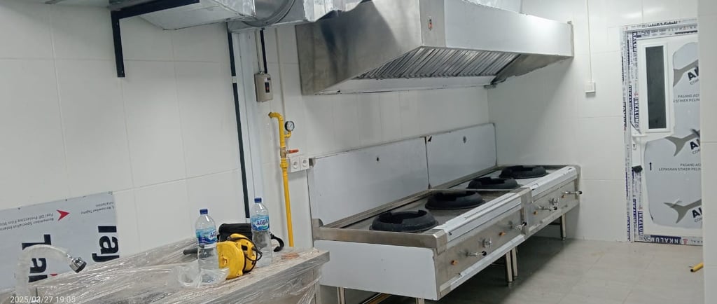 Professional commercial kitchen with stainless steel gas wok ranges and industrial exhaust hood ventilation.