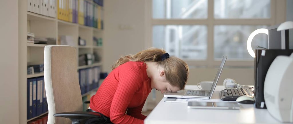 Femme assise à son bureau, penchée vers l’avant, montrant une grande fatigue mentale et physique au travail