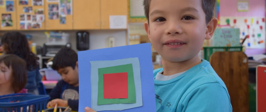 a boy holding a square shaped paper cutout