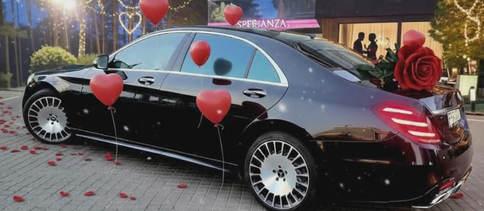 Luxury black Mercedes sedan decorated with red heart balloons and rose petals for a romantic evening event.