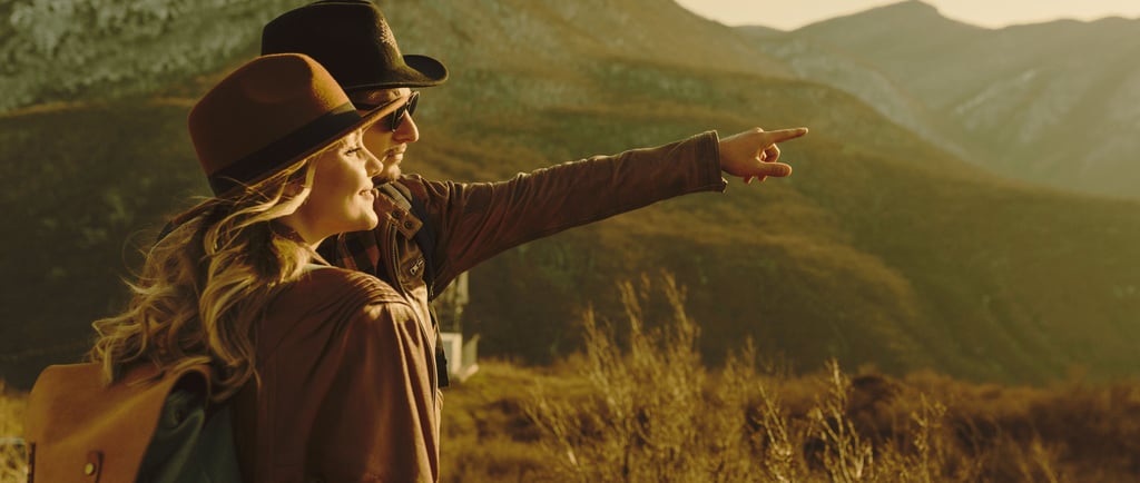 a woman in a hat and a backpack pointing at a mountain