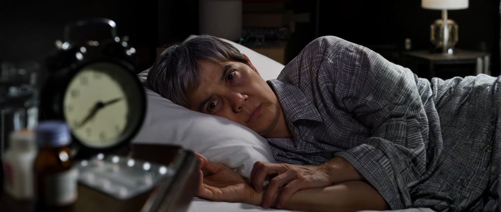 Sleepless person with insomnia lying in bed at night next to an alarm clock and medication.