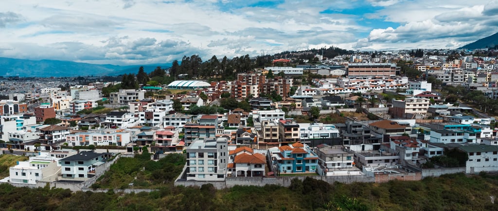 Foto aérea hecha con dron de una pequeña montaña llena de casas y edificios con el cielo azul en Ecuador