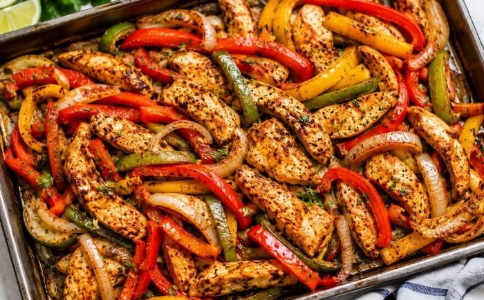 Easy Dump chicken fajitas with roasted bell peppers and onions on a baking tray.