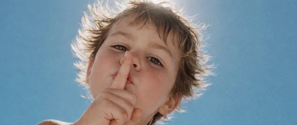 A young child holding a finger to their lips in a hush gesture for confidentiality