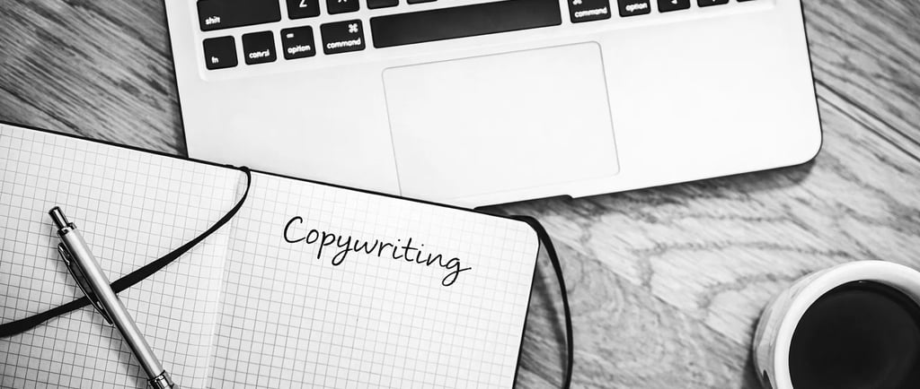Black and white flat lay of a laptop, coffee, and copywriting notebook on a wooden desk.