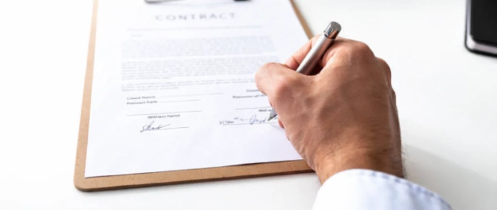 A businessman signs a legal business contract on a clipboard with a silver pen on a white desk.