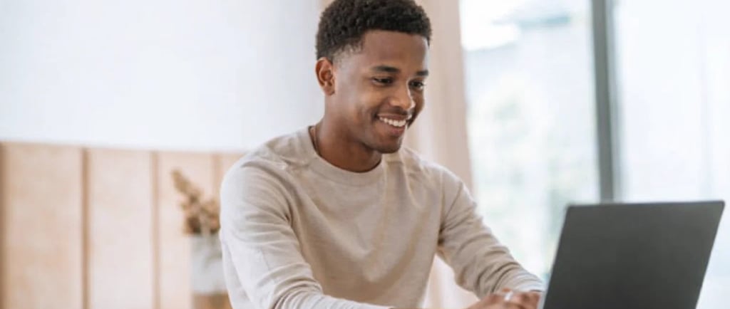 Smiling young Black man working on a laptop at a desk, focused on remote work and digital learning.