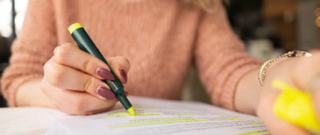 A student using a yellow highlighter to mark important notes on a written document, during revision 