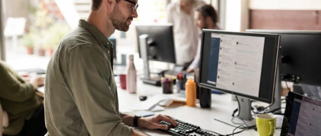 Professional copywriter working on a desktop computer in a modern open-plan office space.