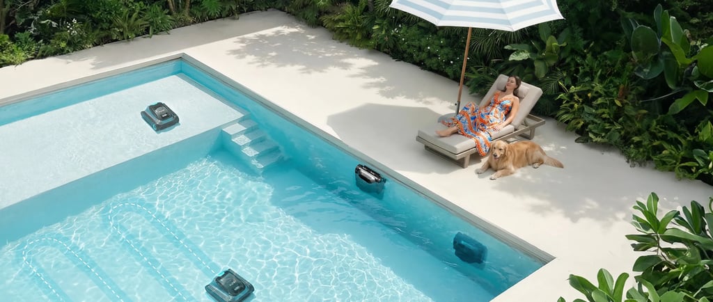 Automatic robotic pool cleaners working in a luxury swimming pool while a woman relaxes nearby.