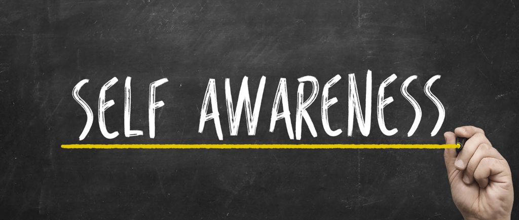 a hand holding a pencil and writing self - awareness on a chalkboard