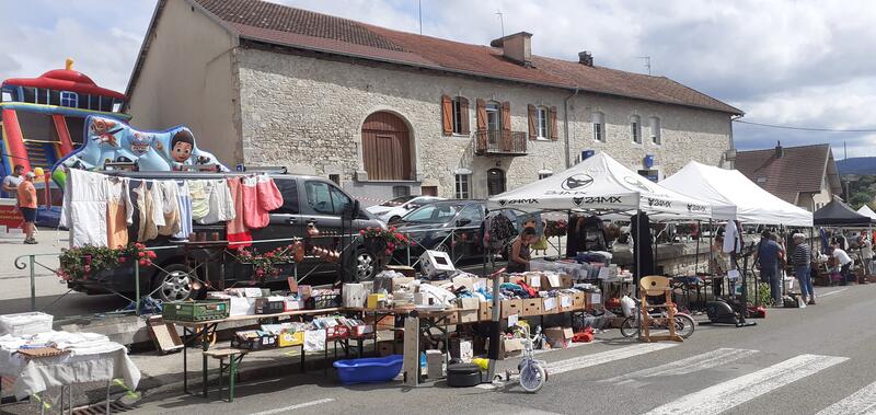 Outdoor flea market stalls with used clothing and household goods in front of a stone building.