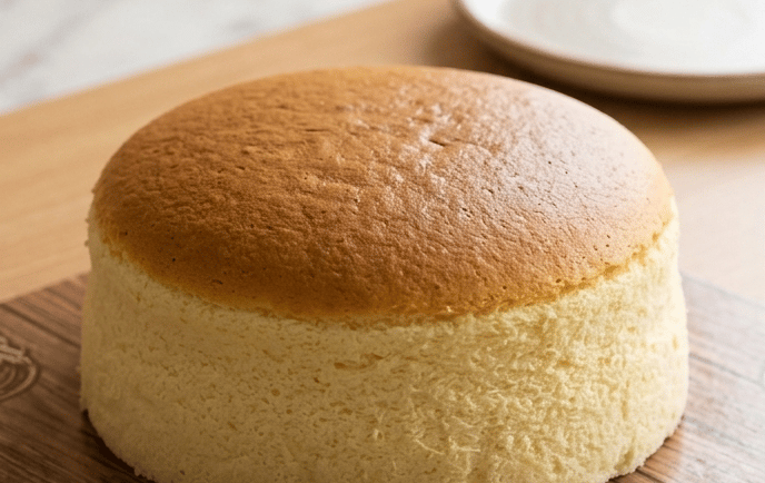 A fluffy Japanese cheesecake with a golden brown top sits on a wooden board.