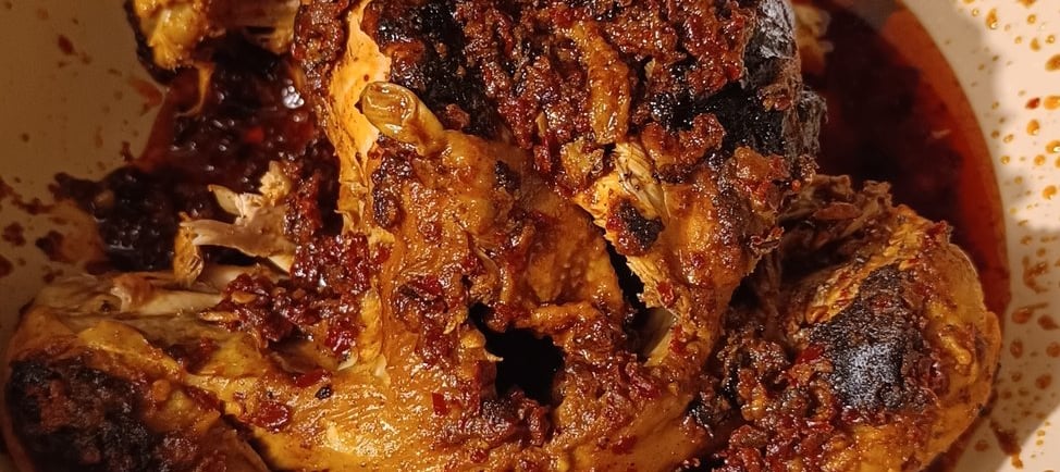 A spicy whole roasted chicken coated in red chili oil and aromatic spices in a white ceramic pan.