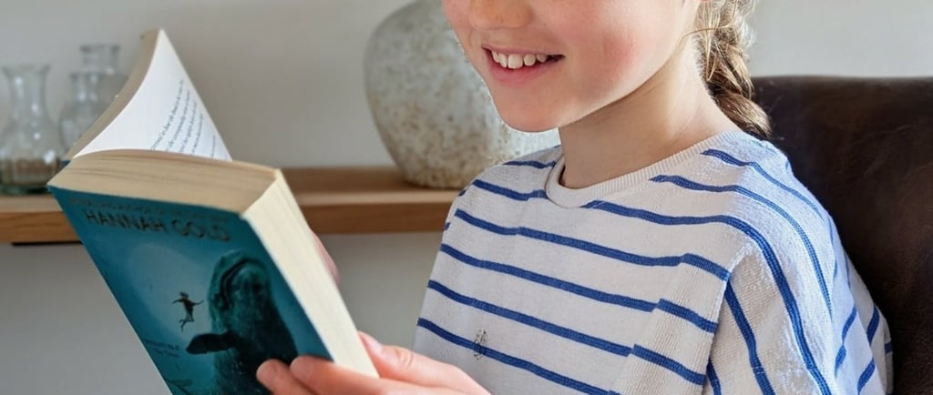 Smiling young girl with braided hair reading a children's book at home titled The Lost Whale.